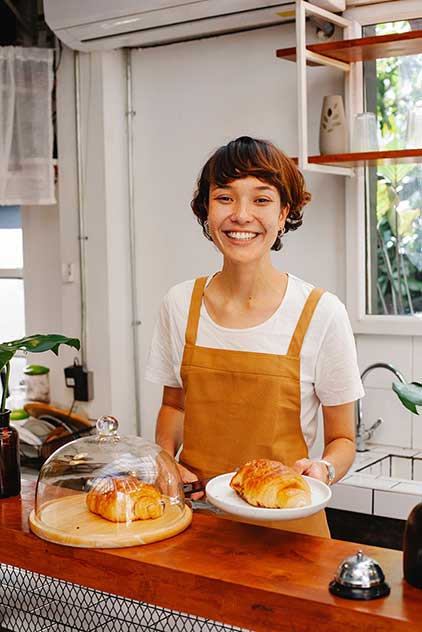 A happy cashier at a French restaurant welcomes customers back. 