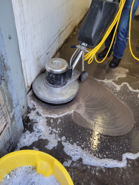 Machine scrubbing of dirty concrete floor.