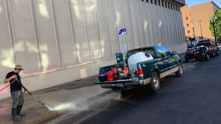 Man uses a truck mounted pressure washer to clean sidewalks.