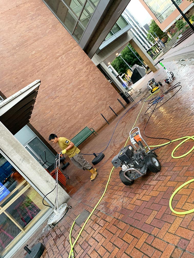 Man pressure washes a restaurant brick courtyard.