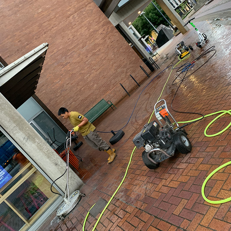 Man commercial pressure washing a brick courtyard.