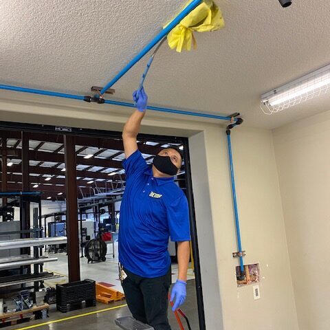 Commercial janitor high dusting ceiling pipes.